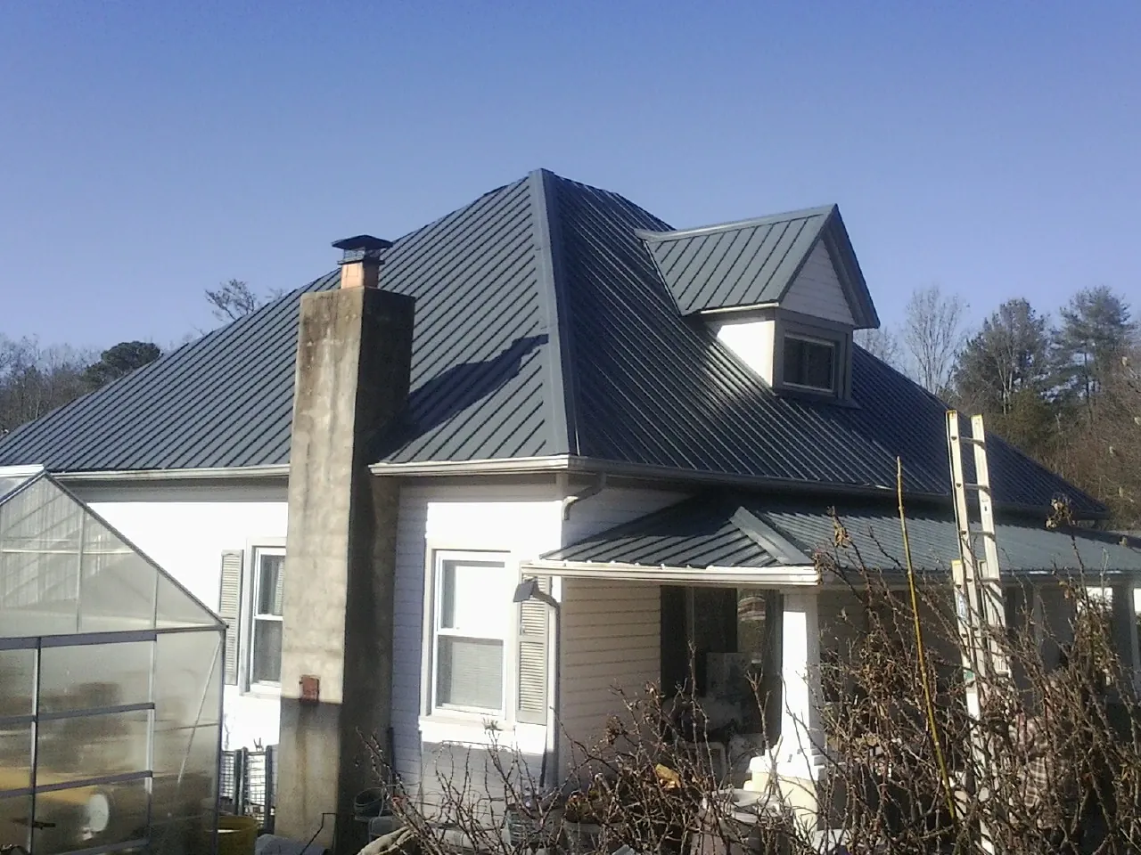Dark blue standing seam metal roof on a white farmhouse with dormer — Slate & Tile Roof Repair by Roofing Brothers in Daleville