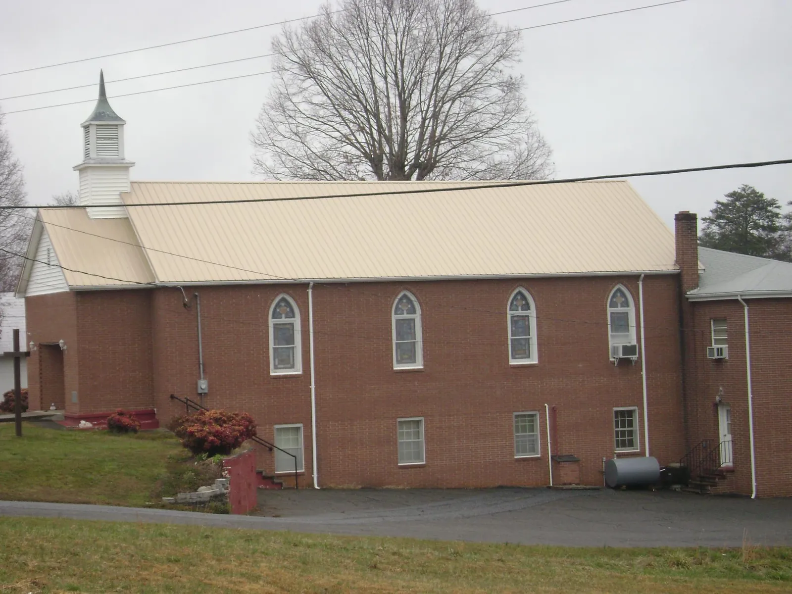 New tan metal roof on a brick church with a white steeple in Daleville