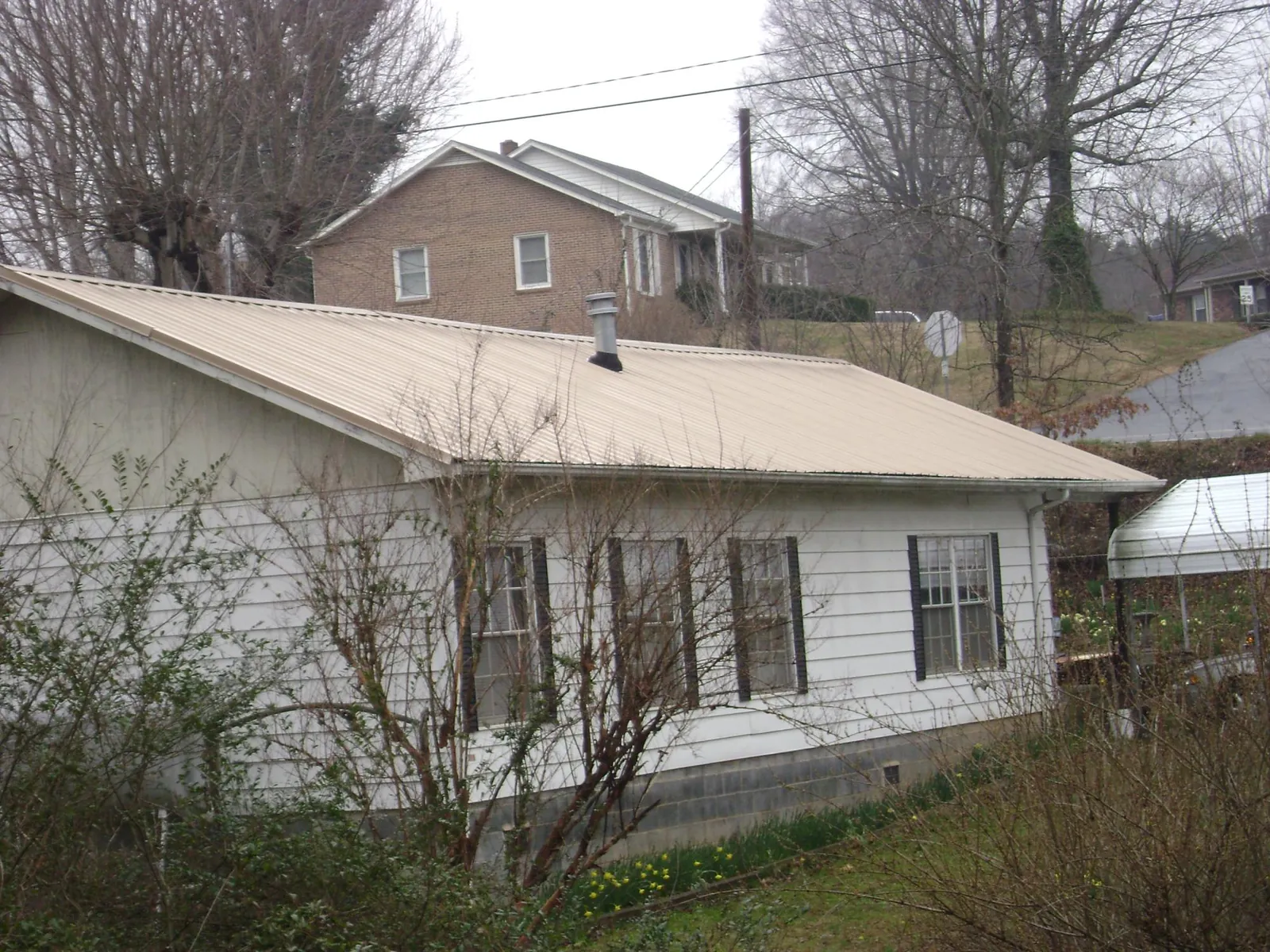 Tan metal roof on a white sided house set into a hillside — Commercial Roofing by Roofing Brothers in Daleville