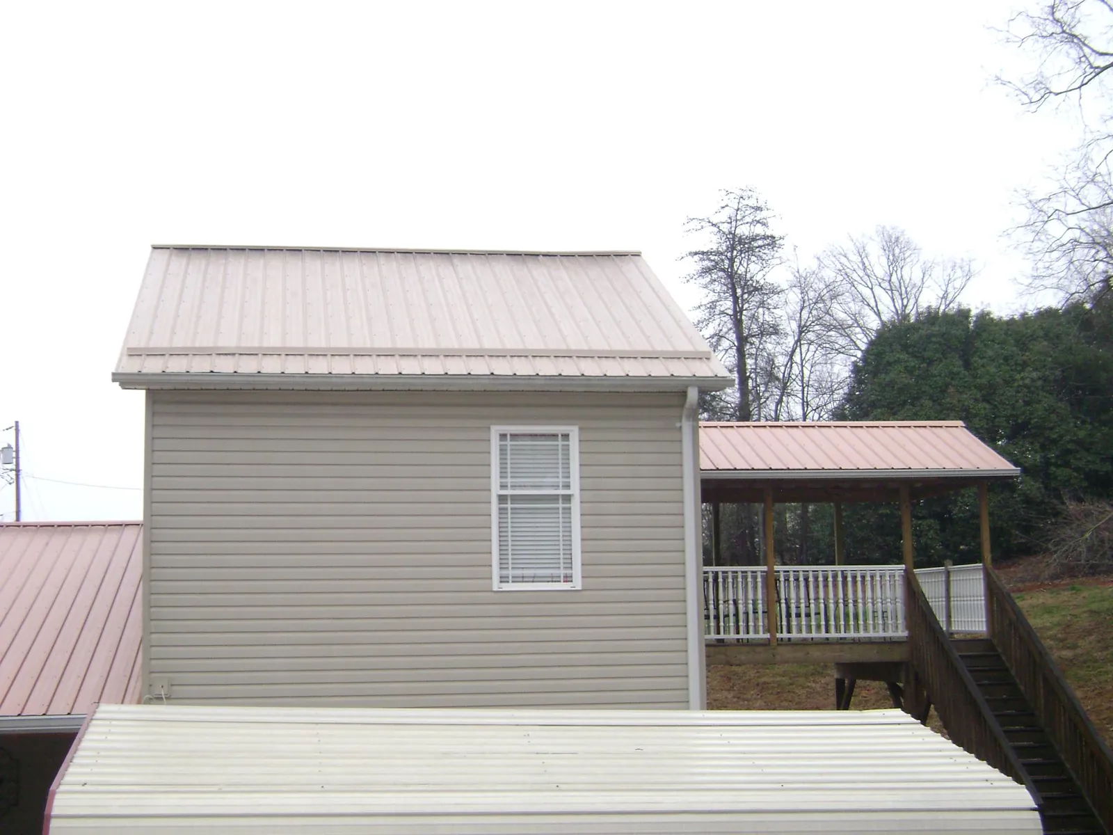 Tan metal roofs on a two story addition and attached porch, from a Roof Replacement job in Daleville